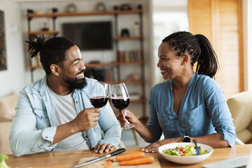 Happy African American couple toasting with wine during lunch at dining table