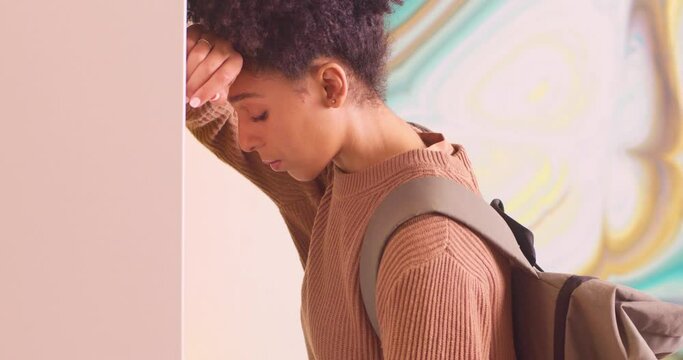 Upset young biracial student leans against lockers, bullying on campus