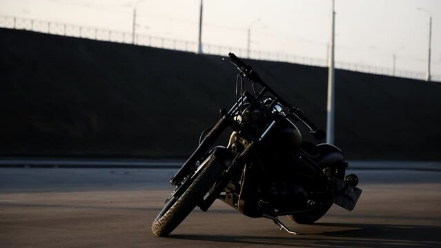 A black chrome motorcycle is parked in the parking lot. Summer evening day. The sun's rays are reflected from the metal chrome parts of the motorcycle. Rare bike. Black motorcycle.
