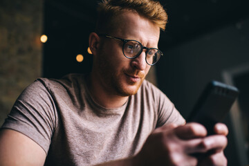 Serious man in eyeglasses using mobile phone in cafeteria