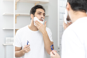 Handsome man looking at the mirror and shaving in the bathroom	