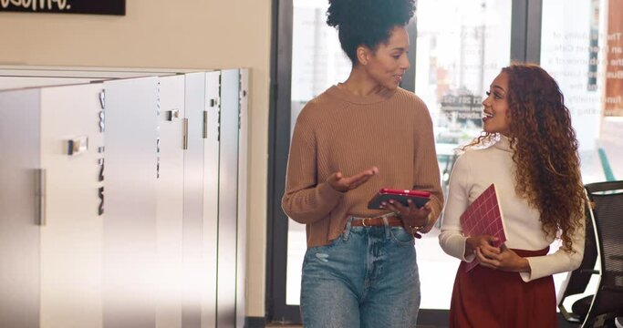 Tracking shot of two multi-ethnic women talking about work, share digital tablet
