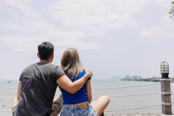 Couple of asian lover hug and hold sitting together looking out to the sea bay.
