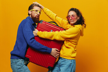 Obraz premium Woman and man smiling, suitcases in hand with yellow and red suitcase smiling merrily and crooked, yellow background, going on a trip, family vacation trip, newlyweds.