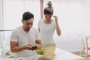 Fototapeta premium Funny asian couple. Wife peeking husband who chatting on the smartphone.