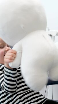 4.5-year-old girl plays in a dental chair with soft toy Lunatic Teletubby or an astronaut she waves it looks smiles relaxed waits for a doctor pediatric dentistry acquaintance protection care