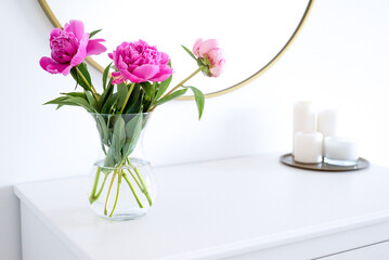 Pink peonies in the apartment. Home decoration, pink peonies on table in white room. Vase with beautiful peony flowers on table in bedroom. Flowers in a vase at home. Mirror reflection, gold frame