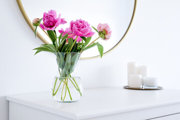 Pink peonies in the apartment. Home decoration, pink peonies on table in white room. Vase with...