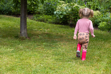 toddler girl spend time outdoor in rubber boots, children have fun in nature - obrazy, fototapety, plakaty