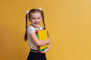 Cheerful schoolgirl holding books against a yellow wall background. The concept of education and school. Space for copying.