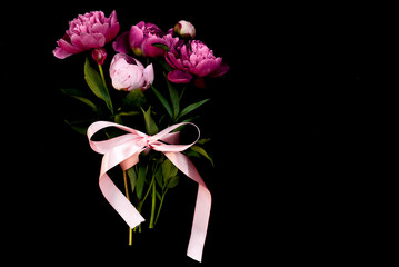 Bouquet of pink Peonies tied with a pink bow. Spring flowers on the white background. Flower arrangement of pink peonies and place for text. Flower bouquet, lat lay. Pink flowers with a ribbon.