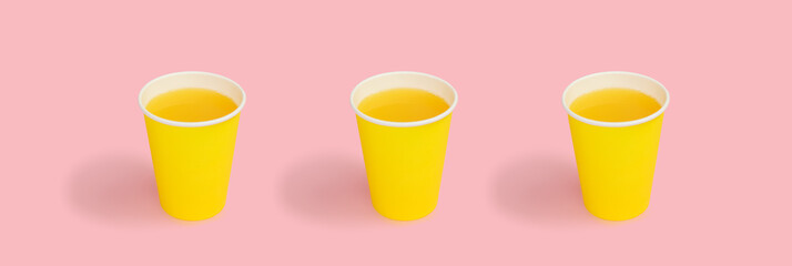 Orange juice in yellow disposable paper cup, against a pink background. Disposable tableware. High...