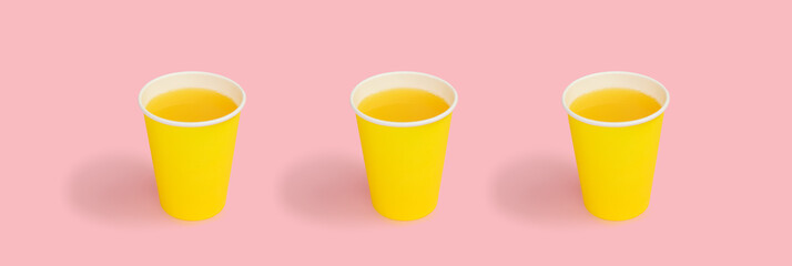 Orange juice in yellow disposable paper cup, against a pink background. Disposable tableware. High quality for summer food and drink photo background, copy space.