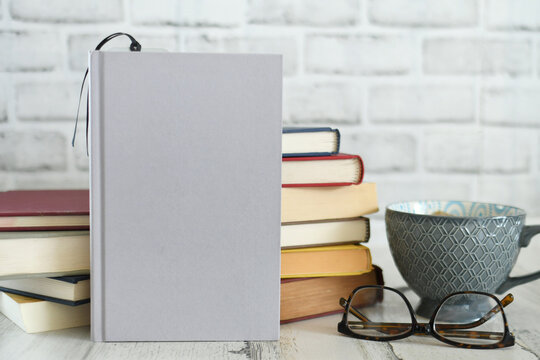 Book cover mock up - plain book against stacks of books with mug & glasses.