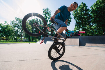A mature tattooed man is balancing on his bmx in a skate park.