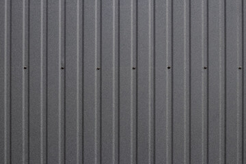 Corrugated surface with the texture of dark gray metal sheet with longitudinal stripes on the wall of an industrial building
