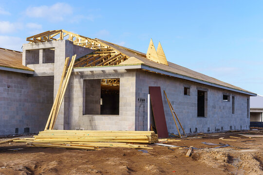 Lumber stacked by concrete shell of a new single-family house with its roof under construction in a suburban development in southwest Florida