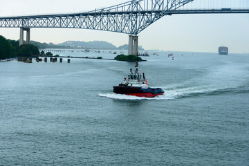 Panama canal tugboat passes under Bridge of the Americas on the Panama canal. Freighter in the...
