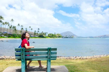 Fototapeten Young woman resting on park bench enjoying the sunshine along Hawaiian ocean © Jaren Wicklund