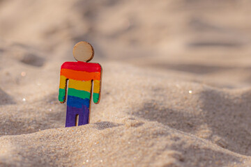 Naklejka premium LGBT wooden people on the beach on the sand. Couple standing on beach with rainbow flag, equal rights, symbol of LGBT community. LGBT flag on a sandy beach. Summer travel concept. A symbol of same-sex