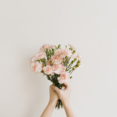 Girl's hand hold elegant pink carnation flowers bouquet on neutral white background. Aesthetic floral, simplicity composition