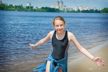 A girl in summer stands in a bathing suit in the summer against the backdrop of the rive