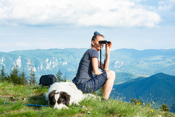Young woman with backpack and holding a binoculars sitting on top of mountain