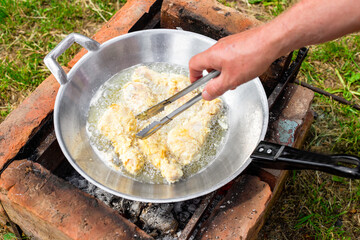a man fries chicken drumsticks in batter in oil in a wok pan at the dacha. Cooking delicious food at a picnic