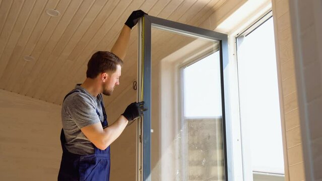Builder worker in uniform installing pvc window with measure tape in wooden modular mobile home