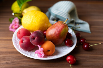 Naklejka na ściany i meble Fresh apricots lemons pears and sweet cherries on the white plate