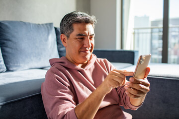 MIddle aged latin man using a smart phone on a couch at home