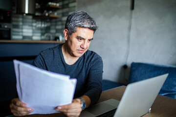 Middle aged man working on his laptop and going over his bills at home