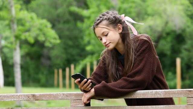 teenage girl in a brown leather jacket with a mobile phone in a summer park