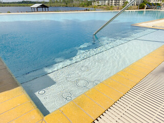 A view of an infinity style swimming pool overlooking a lake, in a Southern Florida landscape.