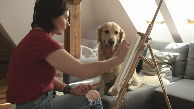 Pretty girl artist drawing sketch with golden retriever dog using pencil and canvas. Beautiful young woman painting portrait of cute doggy pet
