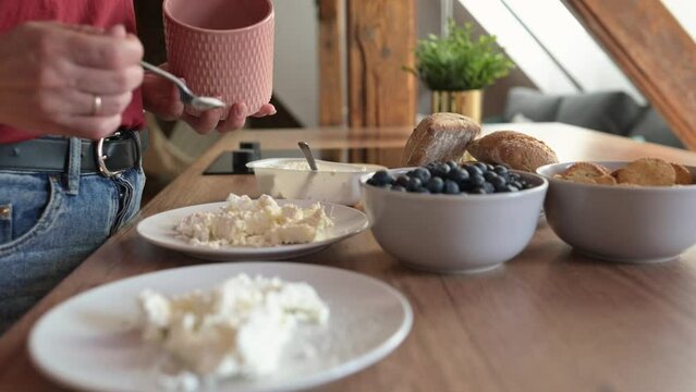 Girl hands put sugar in cottage chease for healthy breakfast at home. Young woman preparing milk cream desert for organic meal nutrition with blueberries