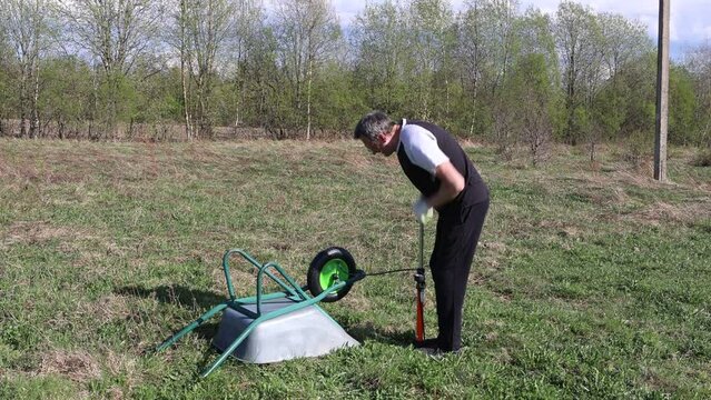 Using manual pneumatic pump to inflate pneumatic tire of one wheel garden wheelbarrow.