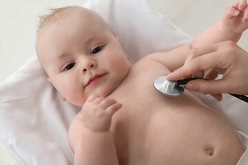 Pediatrician examining cute little baby with stethoscope in clinic, closeup