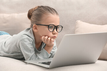 Little girl in glasses with laptop on sofa