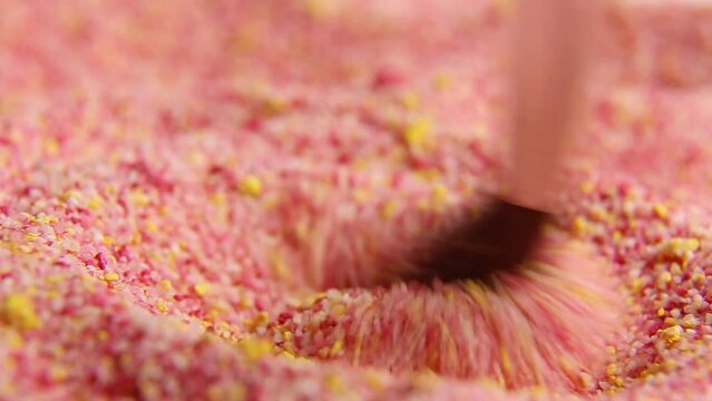 With circular movements of the brush, a powder of color is mixed: crimson yellow. The multicolored powder is gently stirred with a brush. The texture of a red-yellow substance. Macro. ASM video.