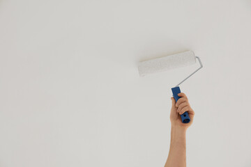 Worker painting ceiling with roller indoors, closeup. Space for text