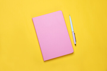 Closed pink notebook and pen on yellow background, flat lay