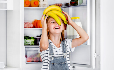 Preteen girl with bananas vitamin healthy food at kitchen. Pretty child kid enjoying yellow fruits...
