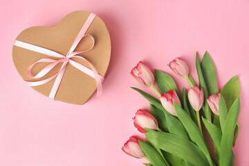 Obraz na płótnie Canvas Heart shaped gift box with bow and beautiful tulips on pale pink background, flat lay