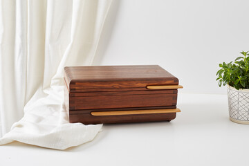 Wooden jewelry box. Product photograph with white cloth and a houseplant.