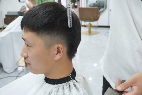 hairdresser makes a haircut for Asian man with a scissors in a barbershop. professional services. beauty salon for men. cosmetics and products for scalp and hair care. close up.