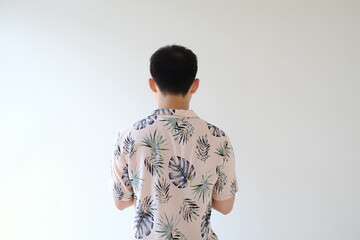Obraz na płótnie Canvas A young Asian man wearing a pink shirt with tropical patterns is standing with his back on the camera. Isolated white background.