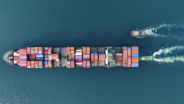 Aerial top view of cargo ship carrying container and running with tug boat for export goods from cargo yard port to custom ocean concept freight shipping by ship
