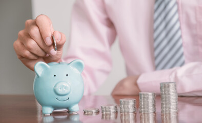 Businessman hand putting coin into blue piggy bank