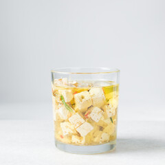 Marinated feta cheese cubes in olive oil in a glass jar. Cheese cubes marinating in olive oil, feta cheese in olive oil with rosemary with dried pepper and tomatoes
